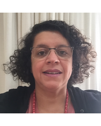 A figura mostra a imagem da professora Isamara Alves Carvalho. Mulher, morena, cabelos curtos, pretos e cacheados, olhos castanhos escuros, com óculos. Está sorrindo. Usa um colar vermelho.
