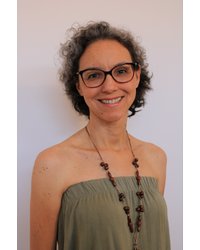 A figura mostra a imagem da professora Thais dos Guimarães Alvim Nunes. Uma mulher com pele clara, olhos castanhos, cabelos curtos, abaixo das orelhas, crespo, castanho e grisalho. Ela está sorrindo. Usa óculos, uma blusa sem alça verde musgo clara e um colar.